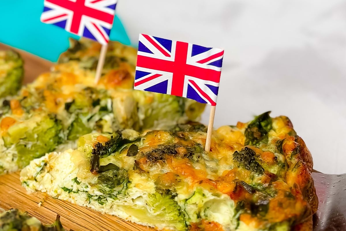 Slices of vegetable quiche with small British flags on wooden board