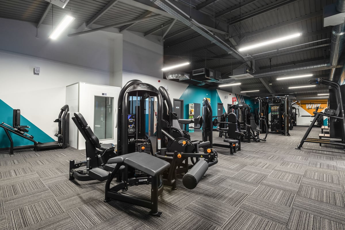 PureGym Llantrisant: Rows of strength training machines, benches, free weights, and rubberized flooring in a gym setting.