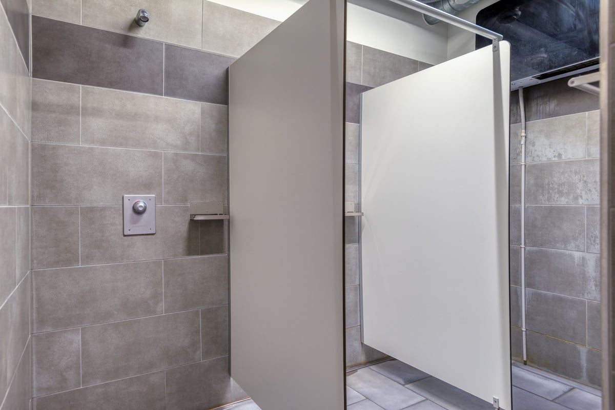 PureGym Lenzburg : vestiaire avec murs carrelés, cabines de douche en verre et casiers.