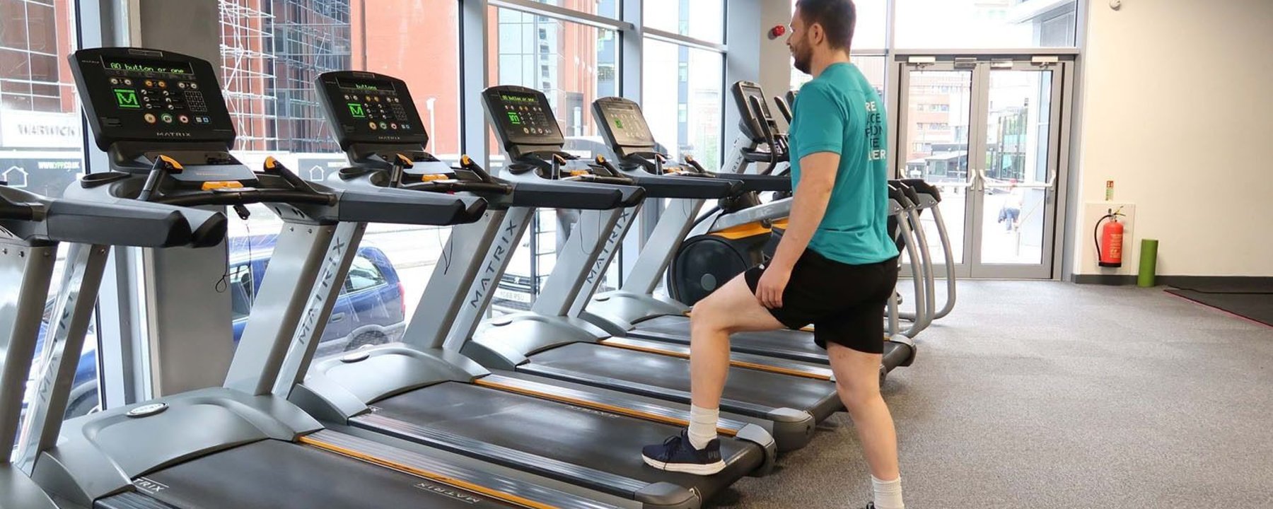 Man in sportswear stretching leg on treadmill in gym with large windows