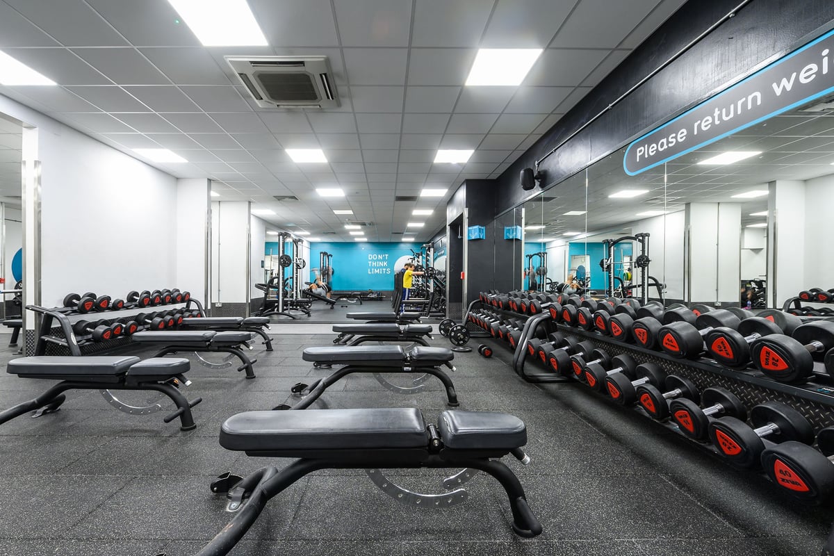 PureGym Burnham: Rows of benches, dumbbells, weight plates, rubberized floors in a bright gym studio.