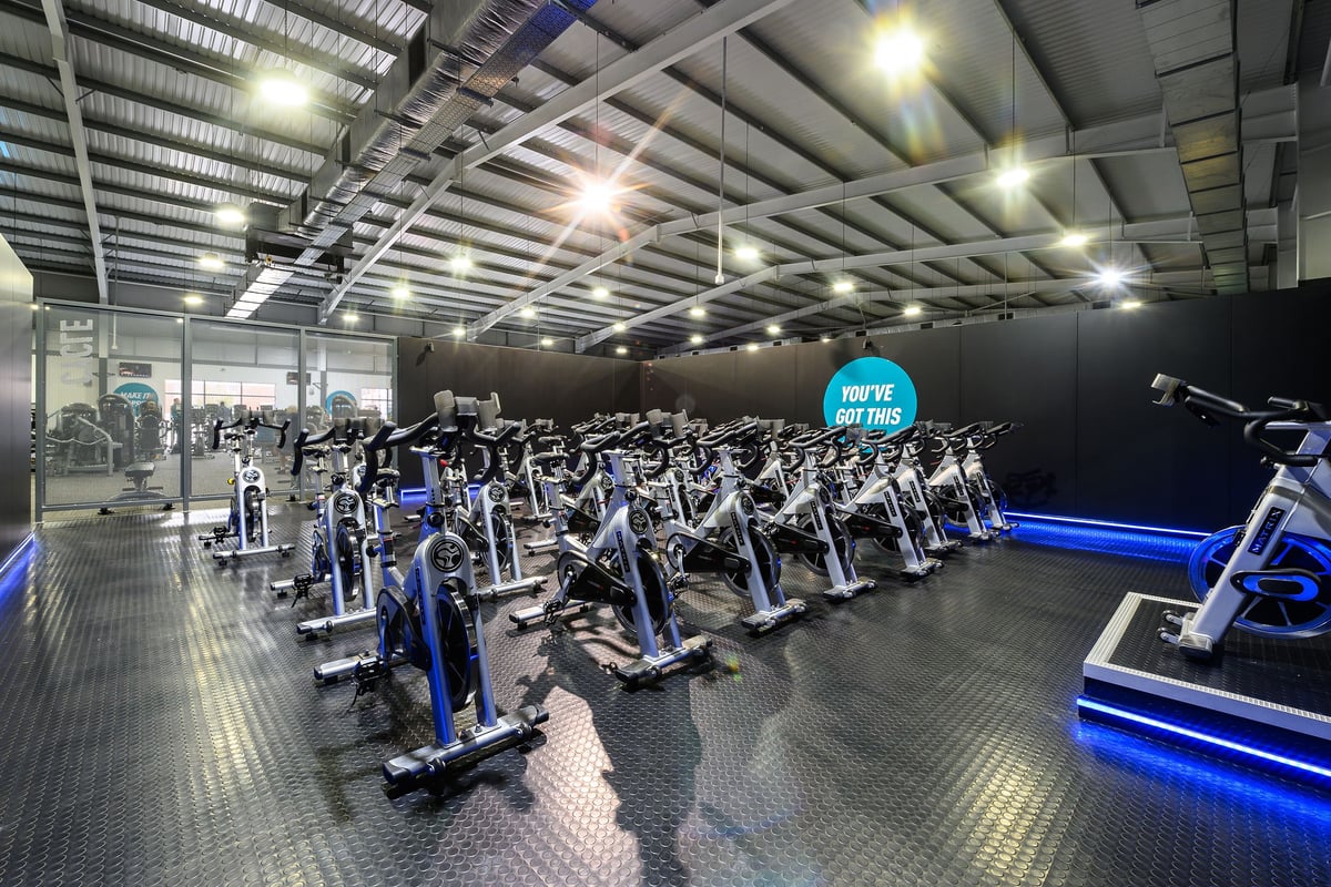 PureGym Widnes: Rows of stationary bikes and treadmills in a well-lit indoor cycling studio.