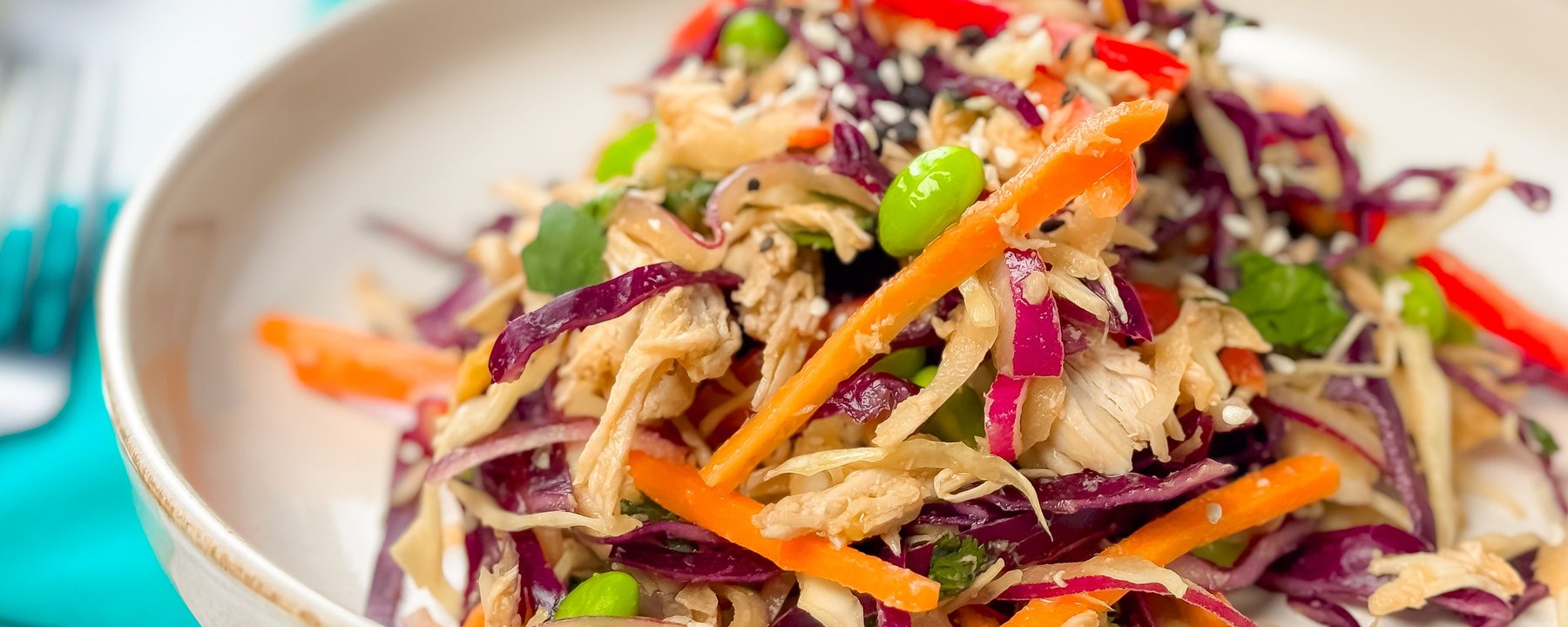 Colourful salad with shredded chicken, purple cabbage, carrots, edamame and sesame seeds