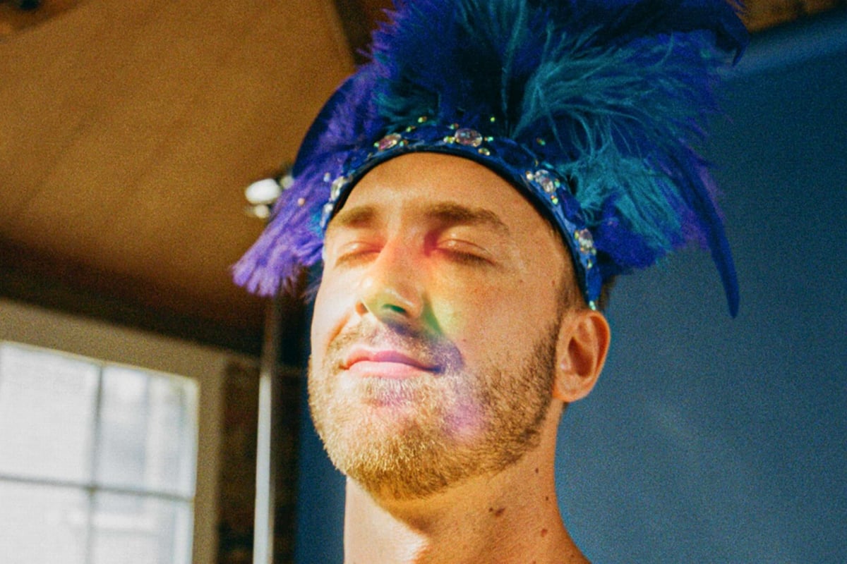 Man with closed eyes wearing a blue feathered headpiece with jewels