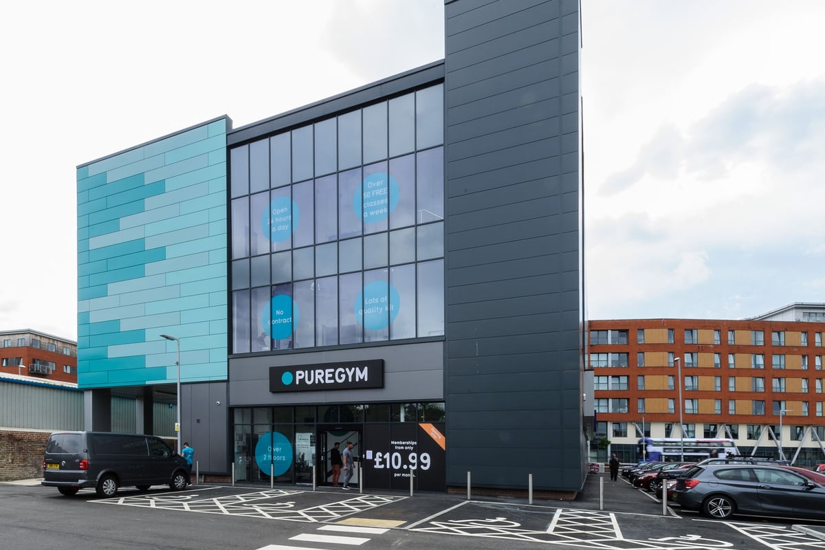 PureGym Leeds Regent Street: Modern gym exterior with teal paneling, ample parking spaces.