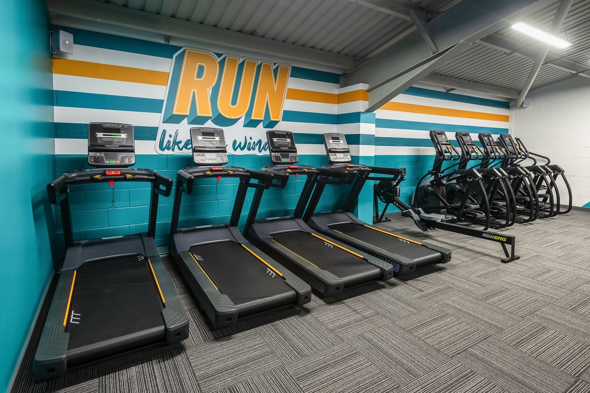 PureGym Llantrisant: Rows of treadmills alongside colourful motivational wall signage in a fitness centre.
