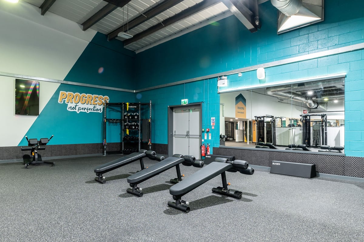 PureGym Lincoln St Marks Centre: Weight benches, barbells, rubberized flooring, teal walls with 'Progress' signage.