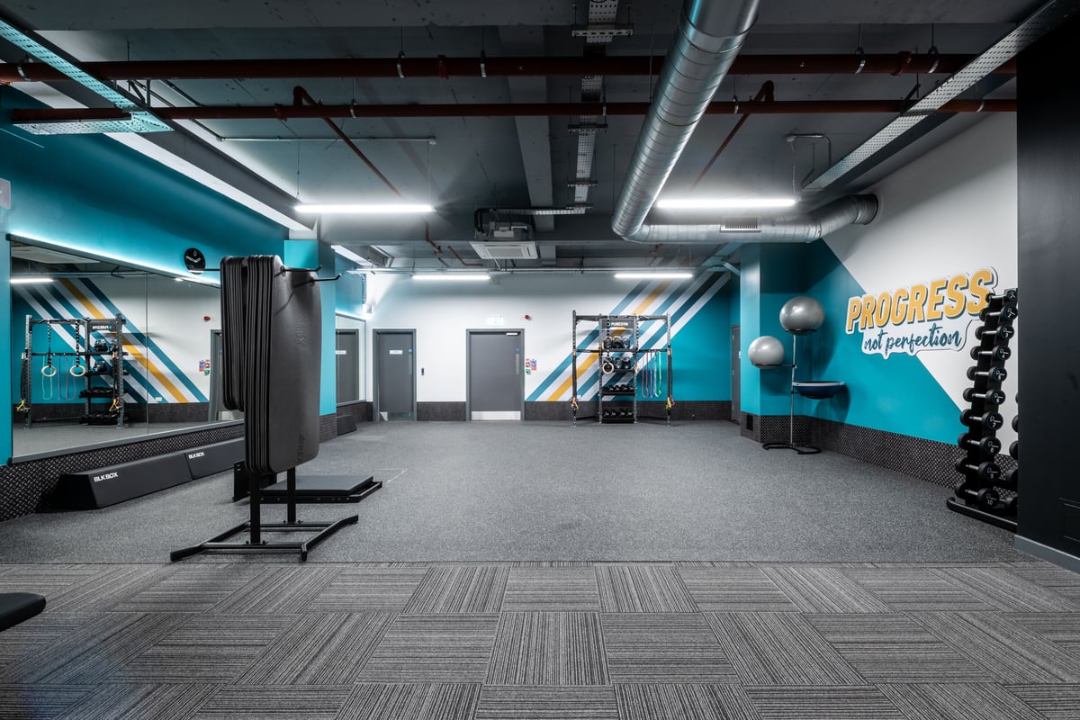 PureGym London Kingston: Resistance training area with squat racks, weight plates, benches, and rubberized flooring.