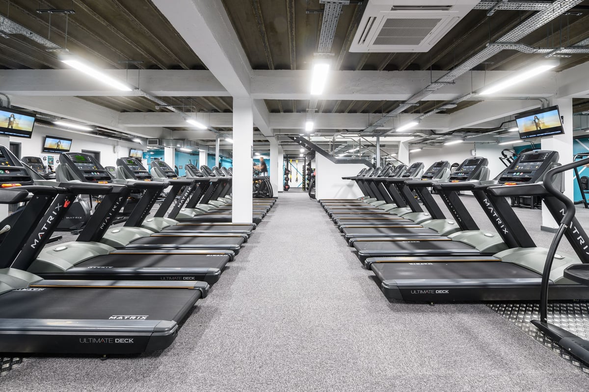 PureGym Brighton London Road: Rows of treadmills bathed in bright light under a ceiling of exposed beams.