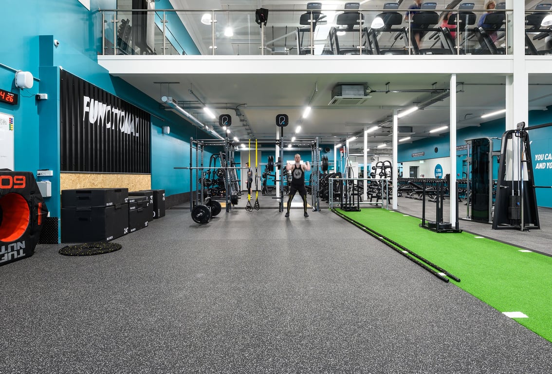 PureGym Exeter Bishops Court: Functional training area with turf, weight racks, rigs, punching bags, rubberized flooring.