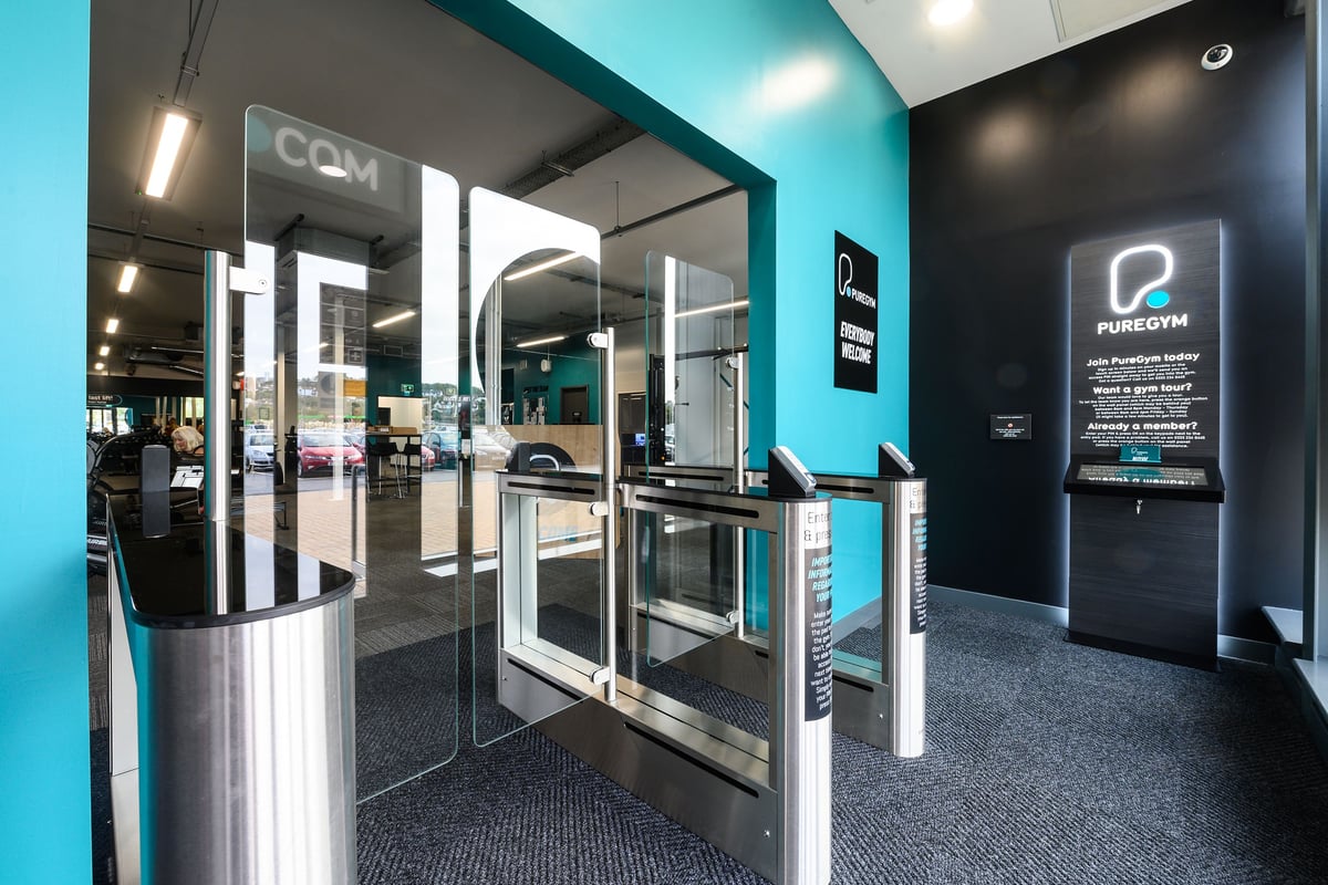 PureGym Barnstaple: Turnstiles, glass walls, and neon lighting indicative of a modern gym entrance area.