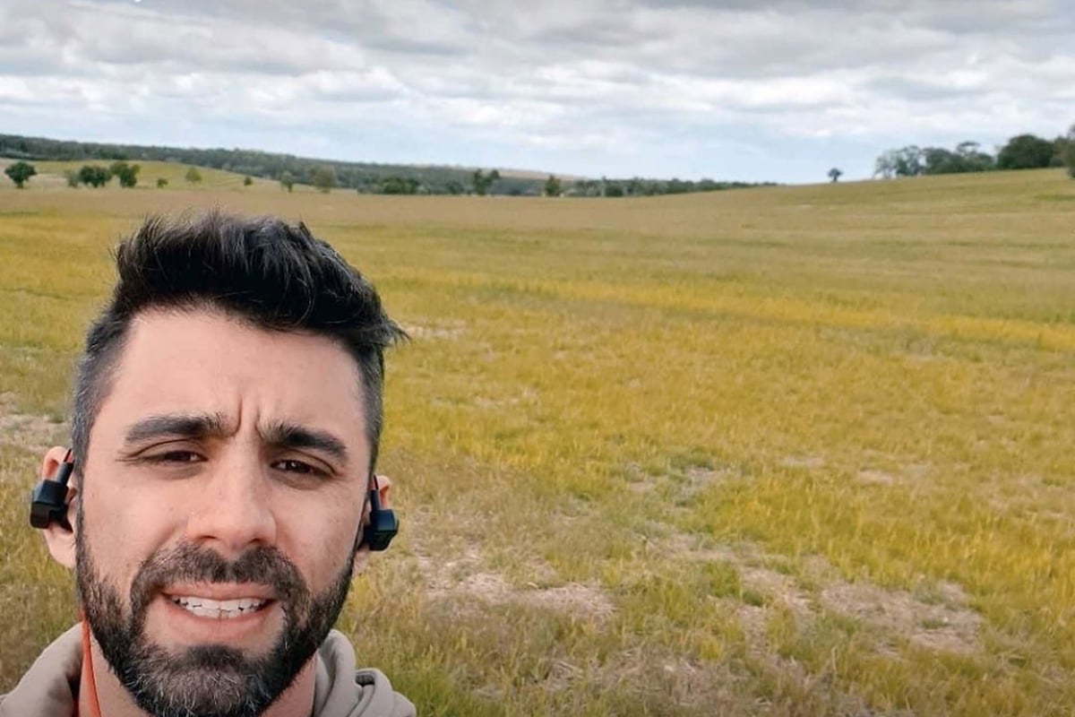 Man with earbuds in a field under a cloudy sky during a walk tracked by Fitbit