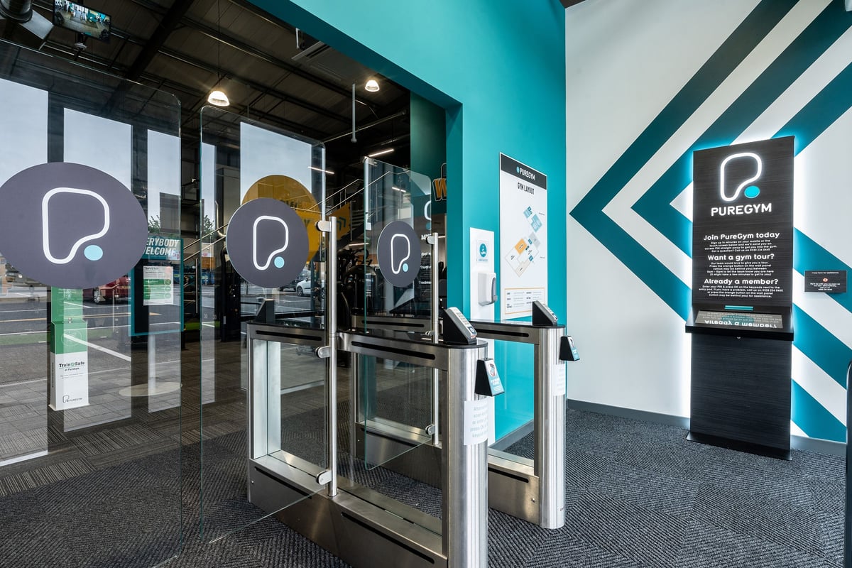 PureGym Cirencester: Glass entrance doors, signage, and self-service kiosks for gym members.