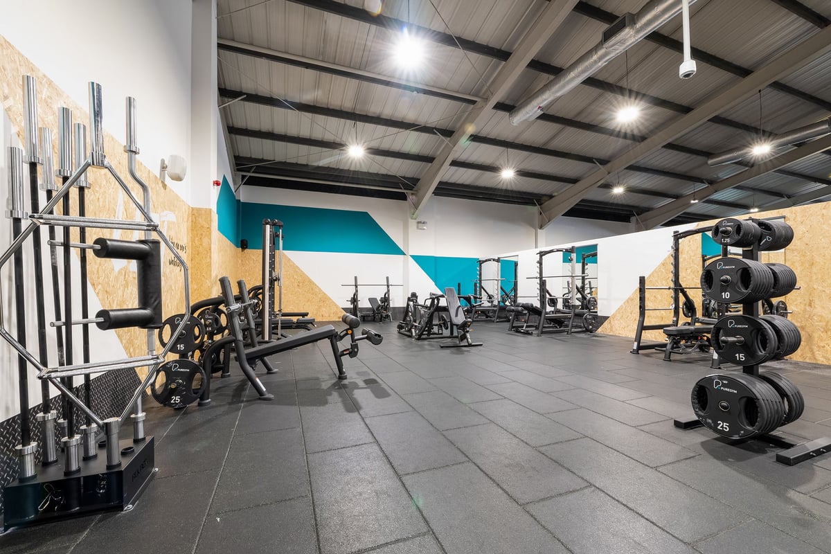 PureGym Leeds Bramley: Fitness studio with weight racks, barbells, squat racks, weight plates, and padded flooring.