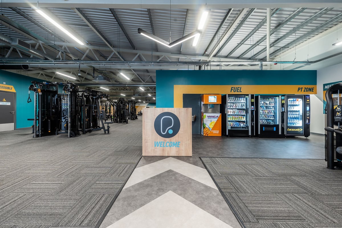 PureGym Barnsley: Vending machines, fitness equipment storage racks, patterned flooring in a gym's utility area.