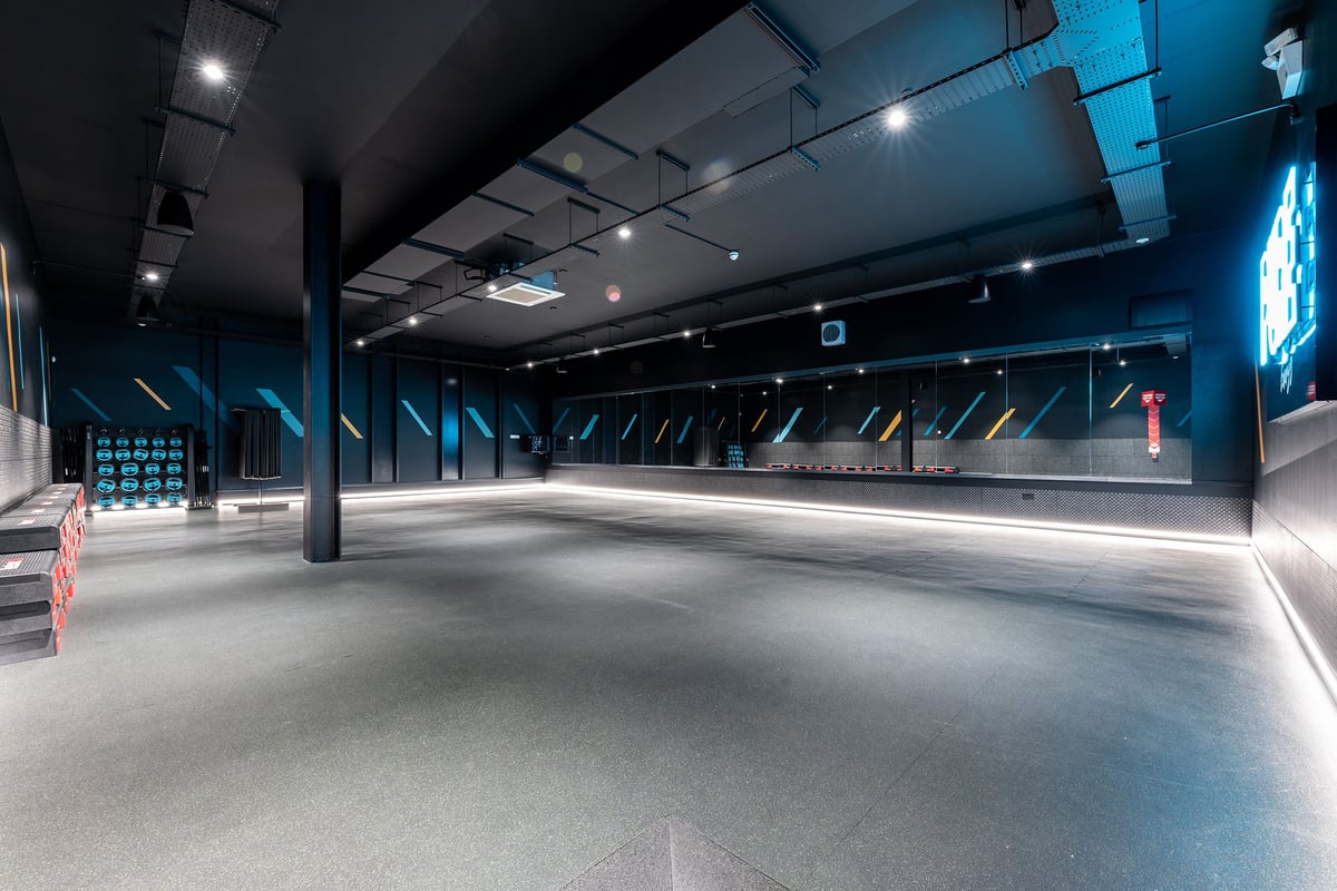 PureGym Nottingham Beeston: Cavernous dimly-lit space with steel beams, concrete floors, and scattered accent lighting.