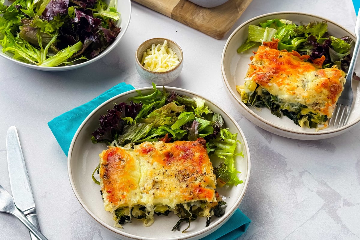 Two plates with spinach lasagne and mixed green salad on a white tablecloth