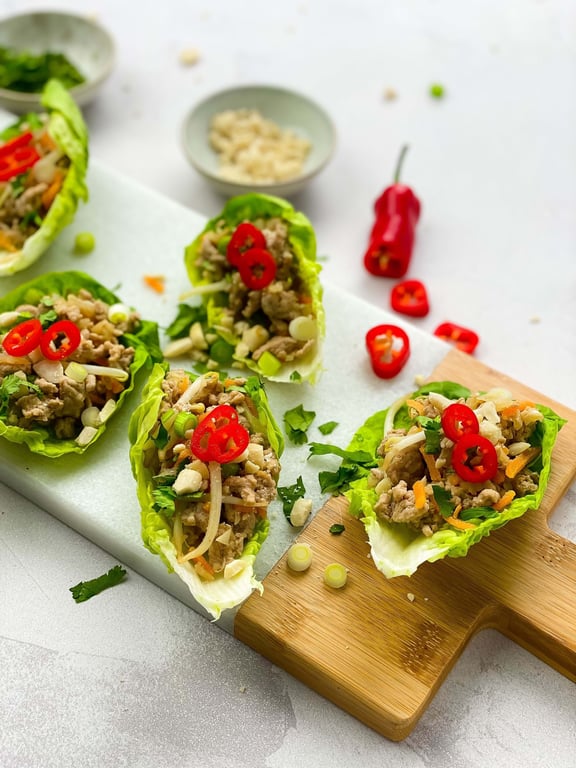 Lettuce wraps filled with minced meat, sliced red chili, spring onions, and herbs on a boa