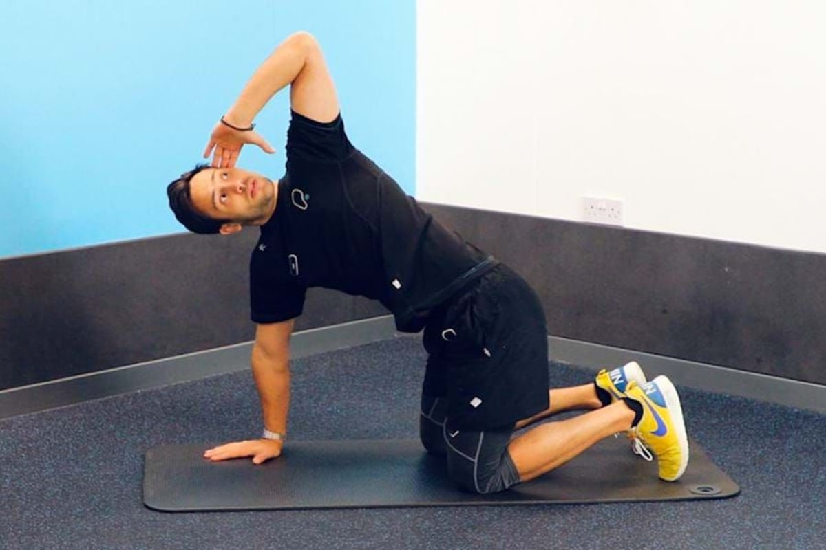 Man in black sportswear stretching on a mat in a corner room with blue and white walls