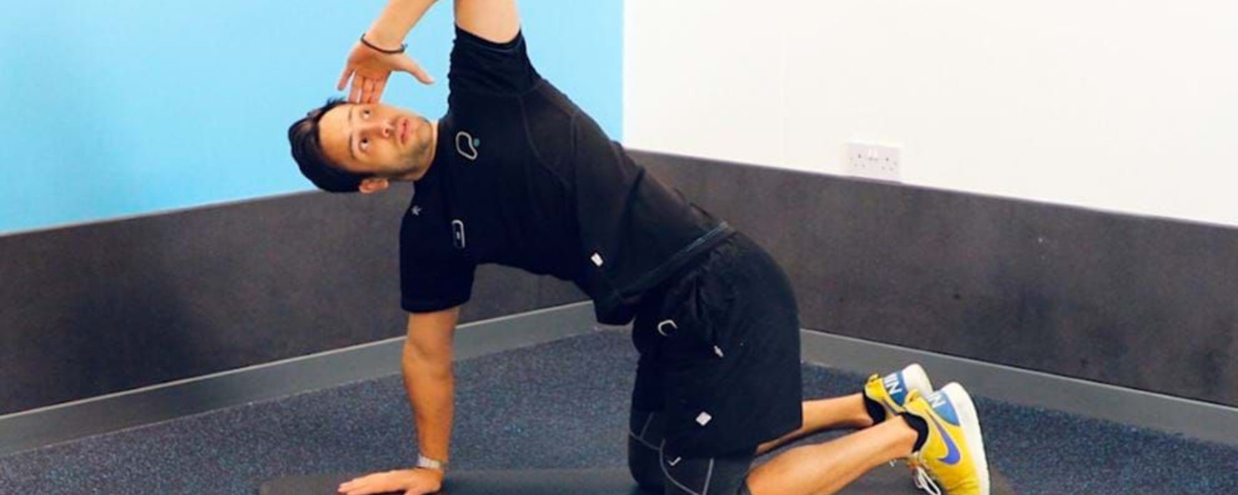 Man in black sportswear stretching on a mat in a corner room with blue and white walls