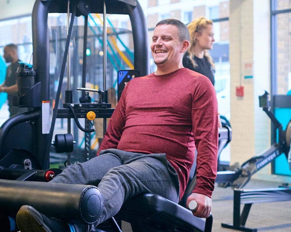 Man in red top exercising legs on gym machine while smiling
