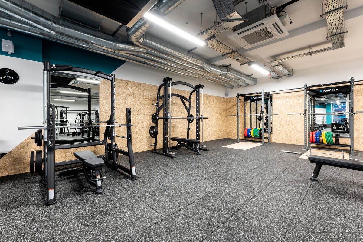 PureGym London Palmers Green: Squat racks, weight plates, rubberized flooring, exposed ducts, and mirrors in a gym studio.