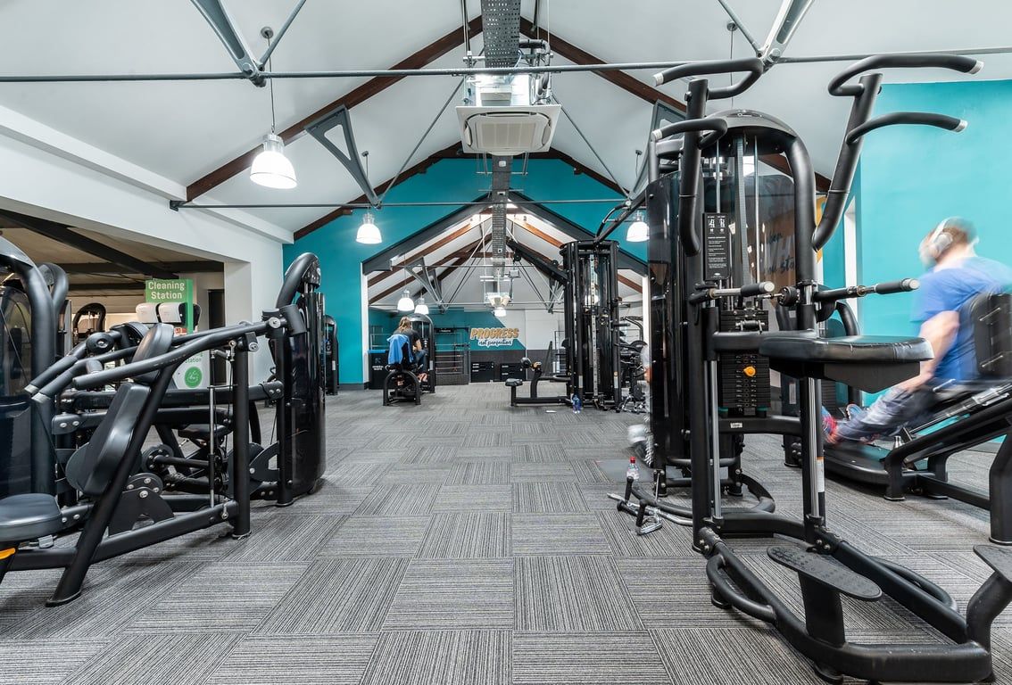 PureGym London Bayswater: Gym interior with exercise machines, weight racks, rubberized flooring, and teal accented walls.