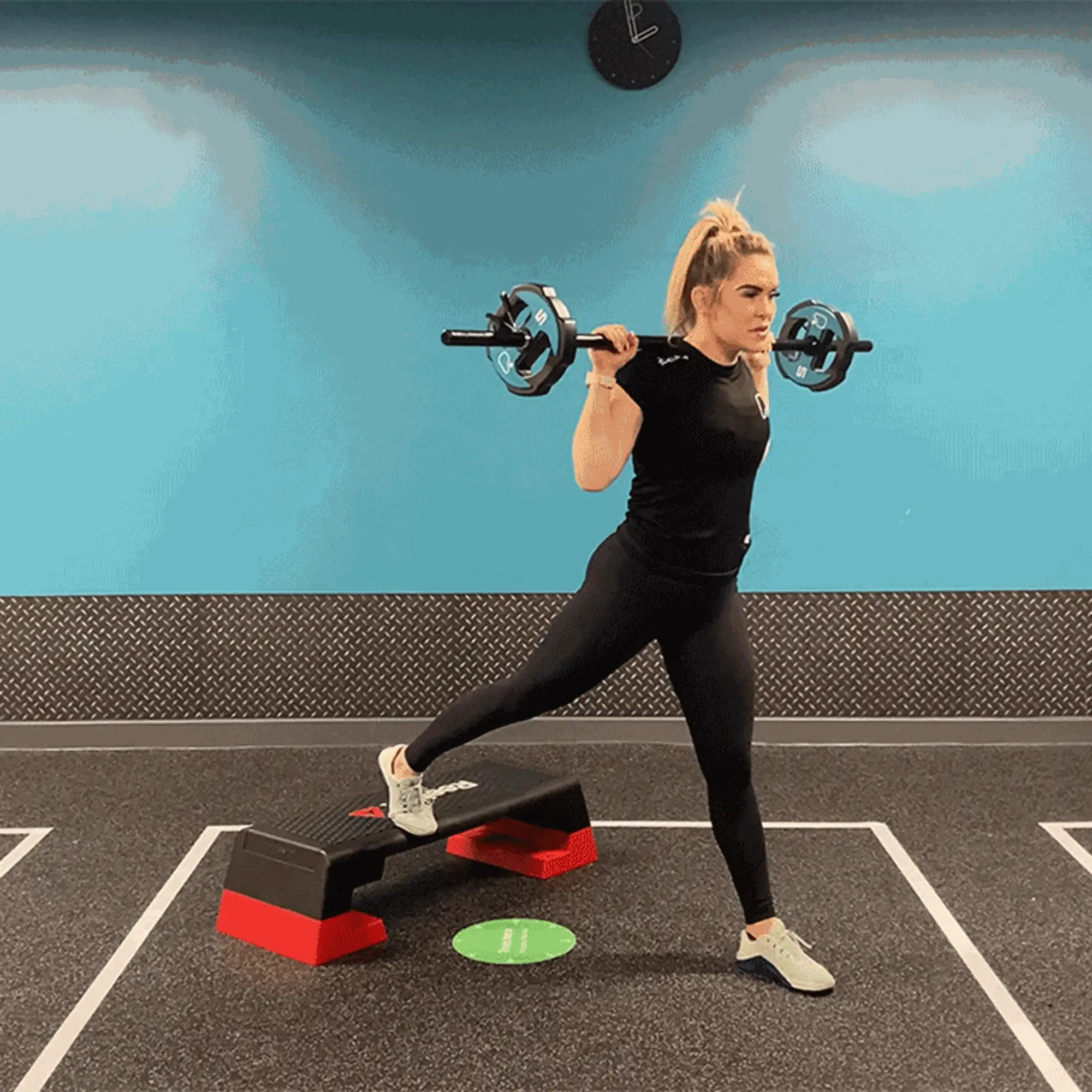 Woman doing split squat with barbell on shoulders in gym with blue wall