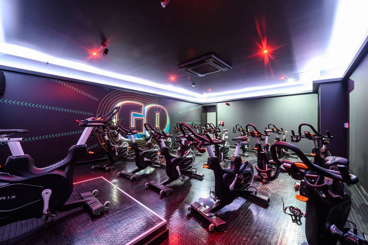 PureGym London East Sheen: Rows of stationary bikes in a dimly lit studio with neon accents and motivational branding.