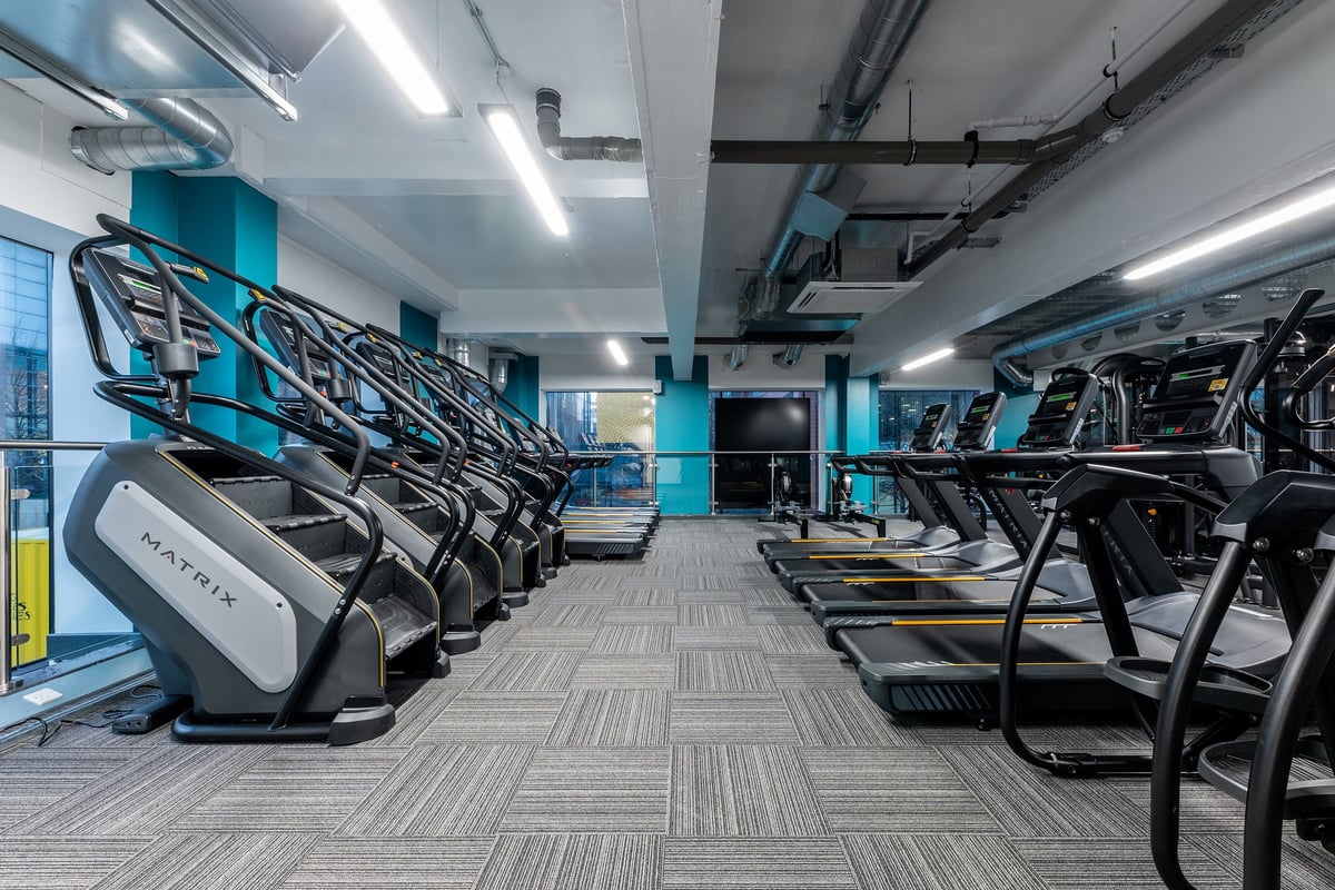 PureGym Manchester First Street: Rows of treadmills and exercise bikes in a modern gym with blue lighting accents.