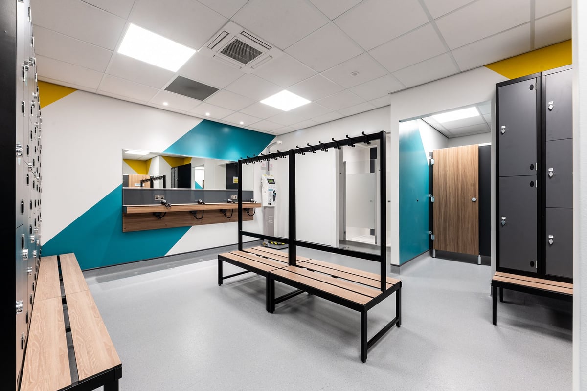 PureGym Dewsbury: Locker room with benches, partitions, lockers, and a vanity counter.