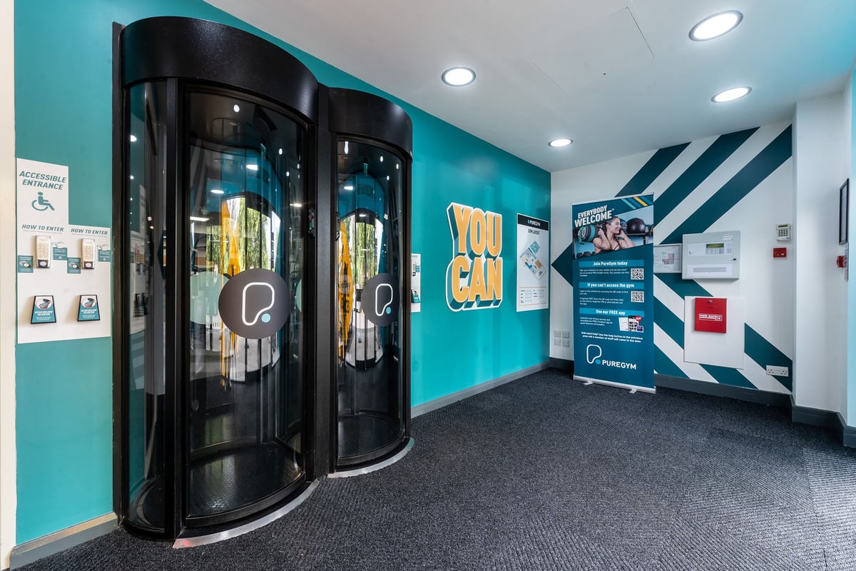 PureGym Woking: Revolving doors to enter a gym, teal walls, equipment display graphics.