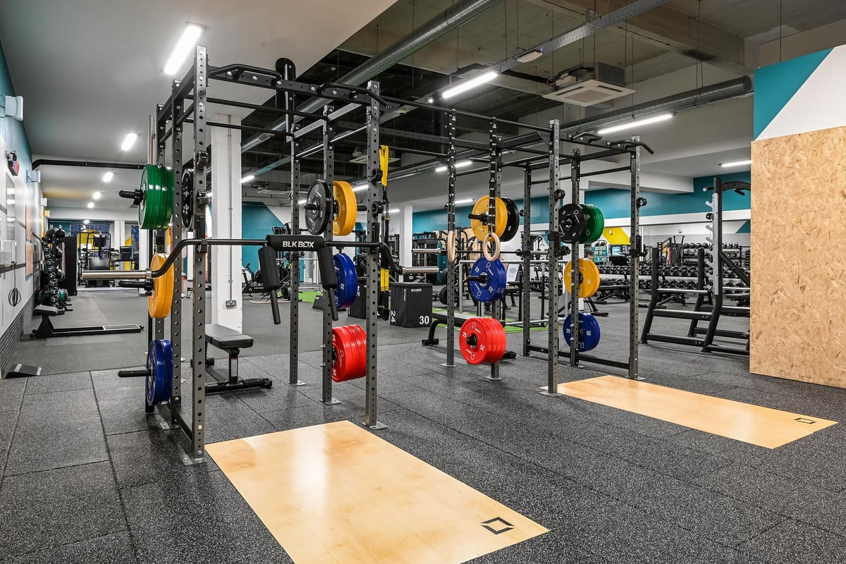 PureGym London Bethnal Green: Squat racks, weight plates in various colours, rubberized flooring in an indoor gym setting.