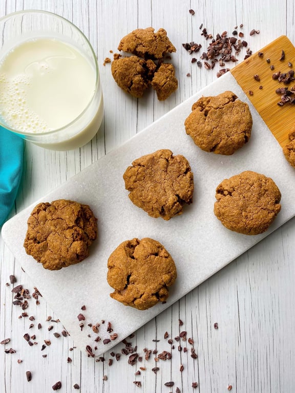 Glass of milk next to six chocolate chip cookies on a white marble board