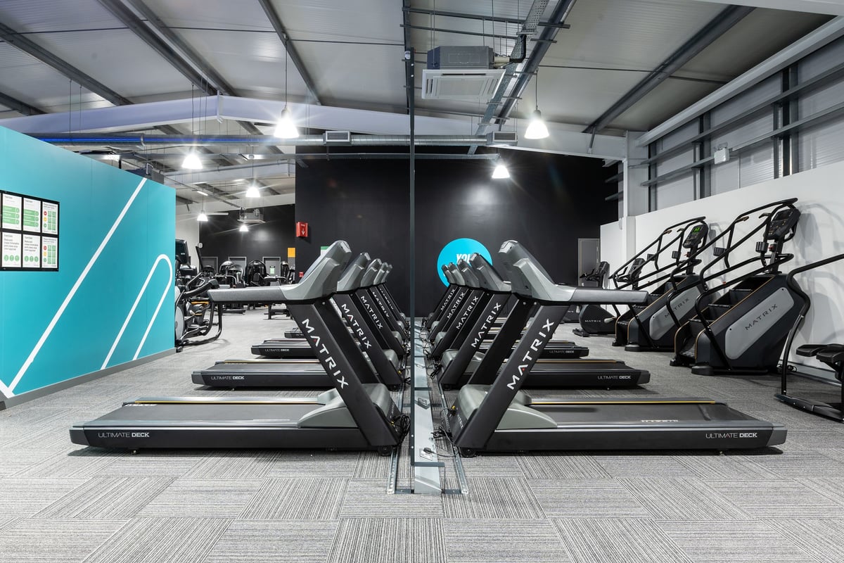 PureGym Andover: Rows of treadmills, sleek black-framed exercise machines, teal accent walls, and rubberised flooring.