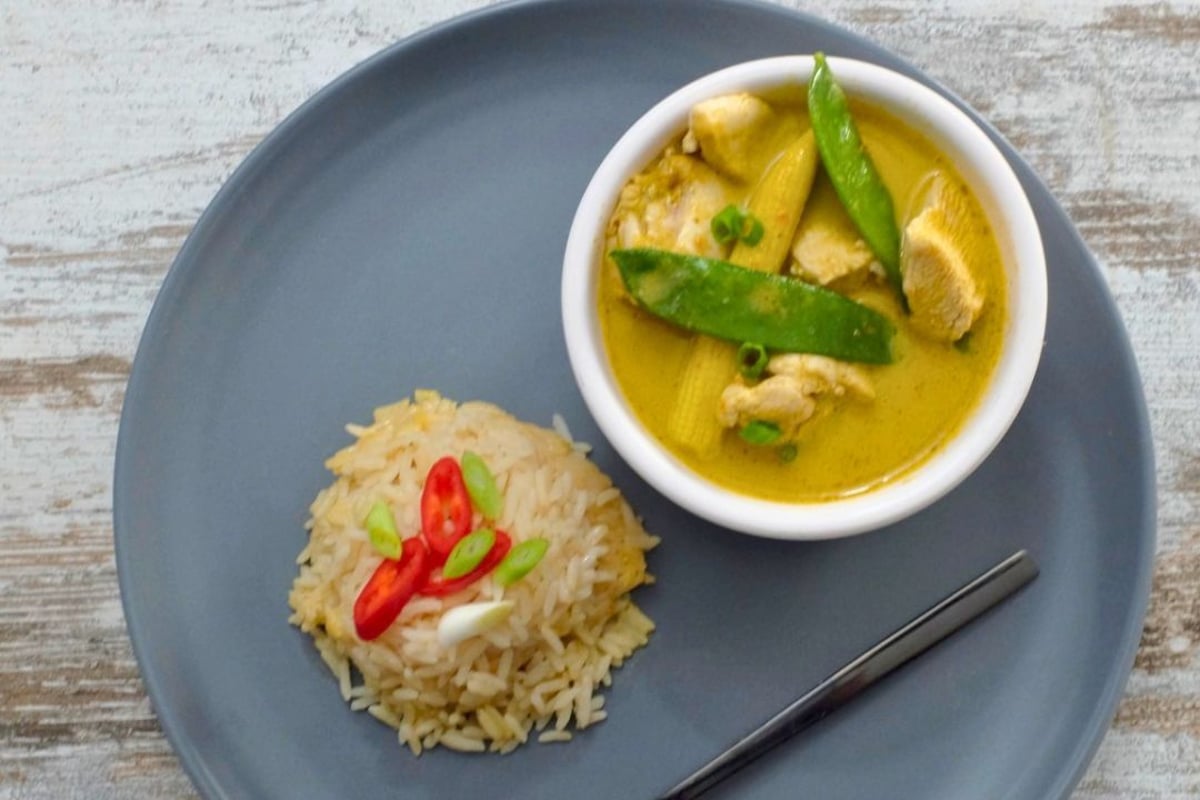 Bowl of Thai red curry with vegetables in a creamy red coconut sauce, garnished with fresh herbs and served with rice.
