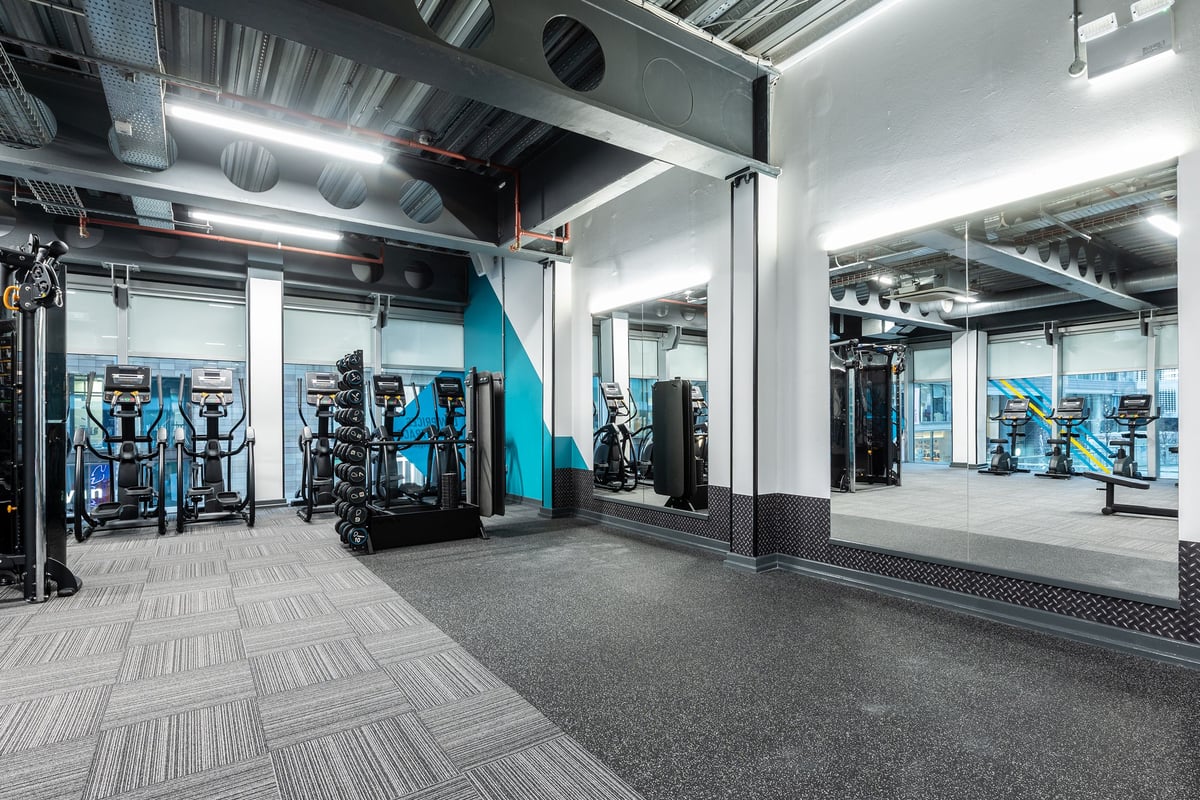 PureGym Manchester Spinningfields: Resistance machine area with racks, benches, mirrored walls, and industrial fit-out.