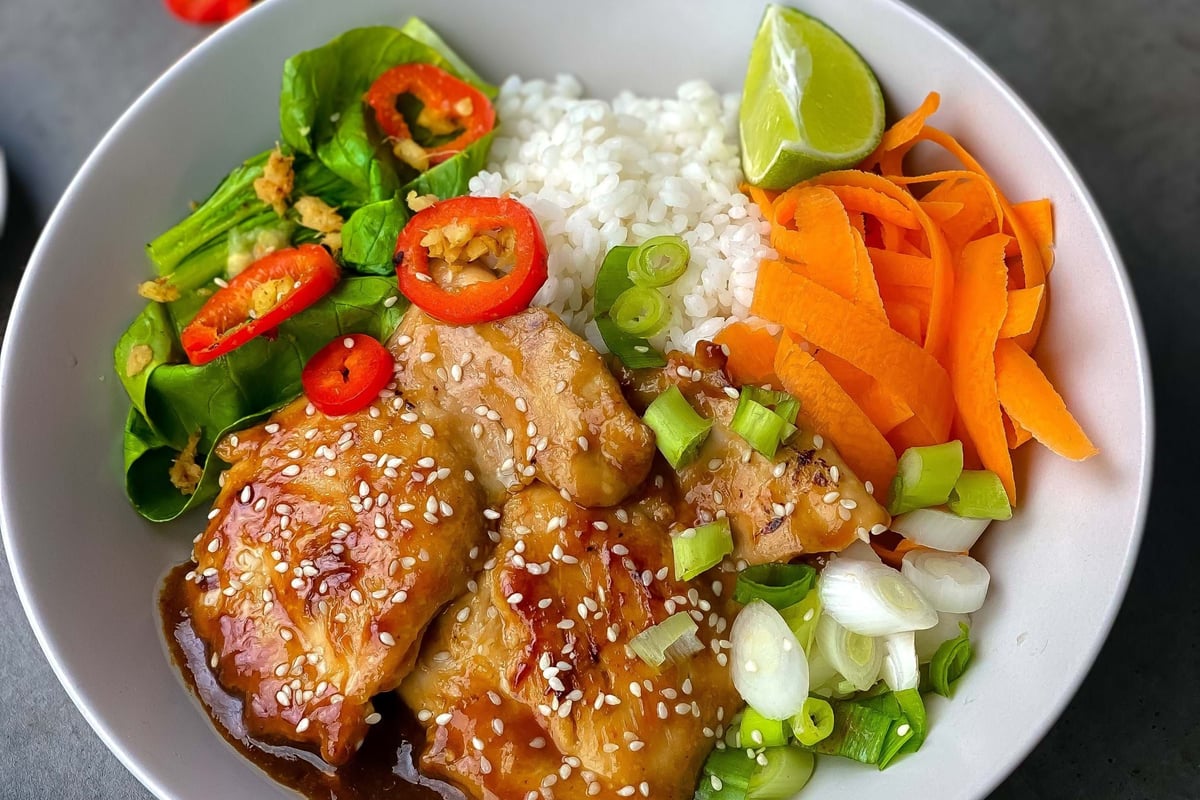 Chicken with sesame seeds, rice, carrot ribbons, greens, spring onions, and lime wedge in
