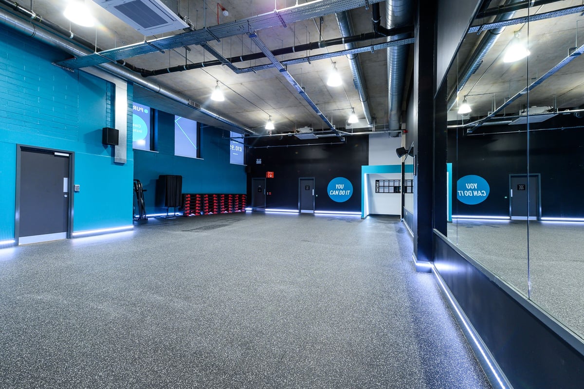 PureGym London Kidbrooke Village: Weightlifting area with rubberized flooring, mirrored walls, and colourful weight plates.