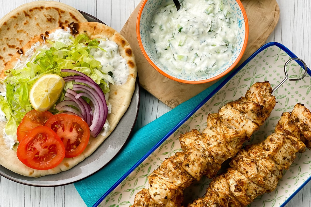 Grilled chicken skewers on rectangular plate with flatbread topped with salad and sauce