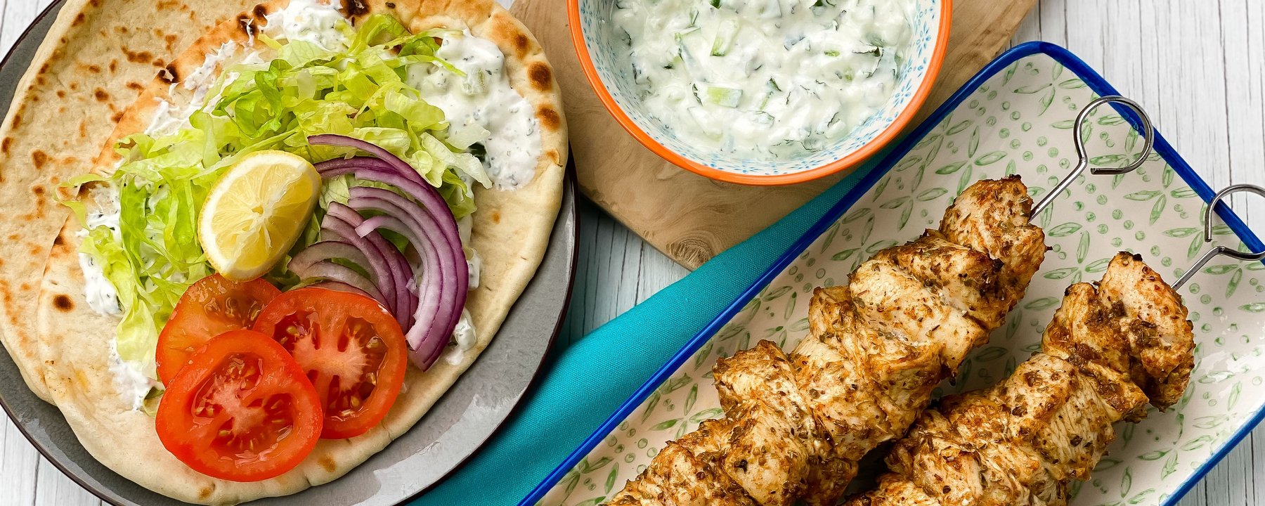 Grilled chicken skewers on rectangular plate with flatbread topped with salad and sauce