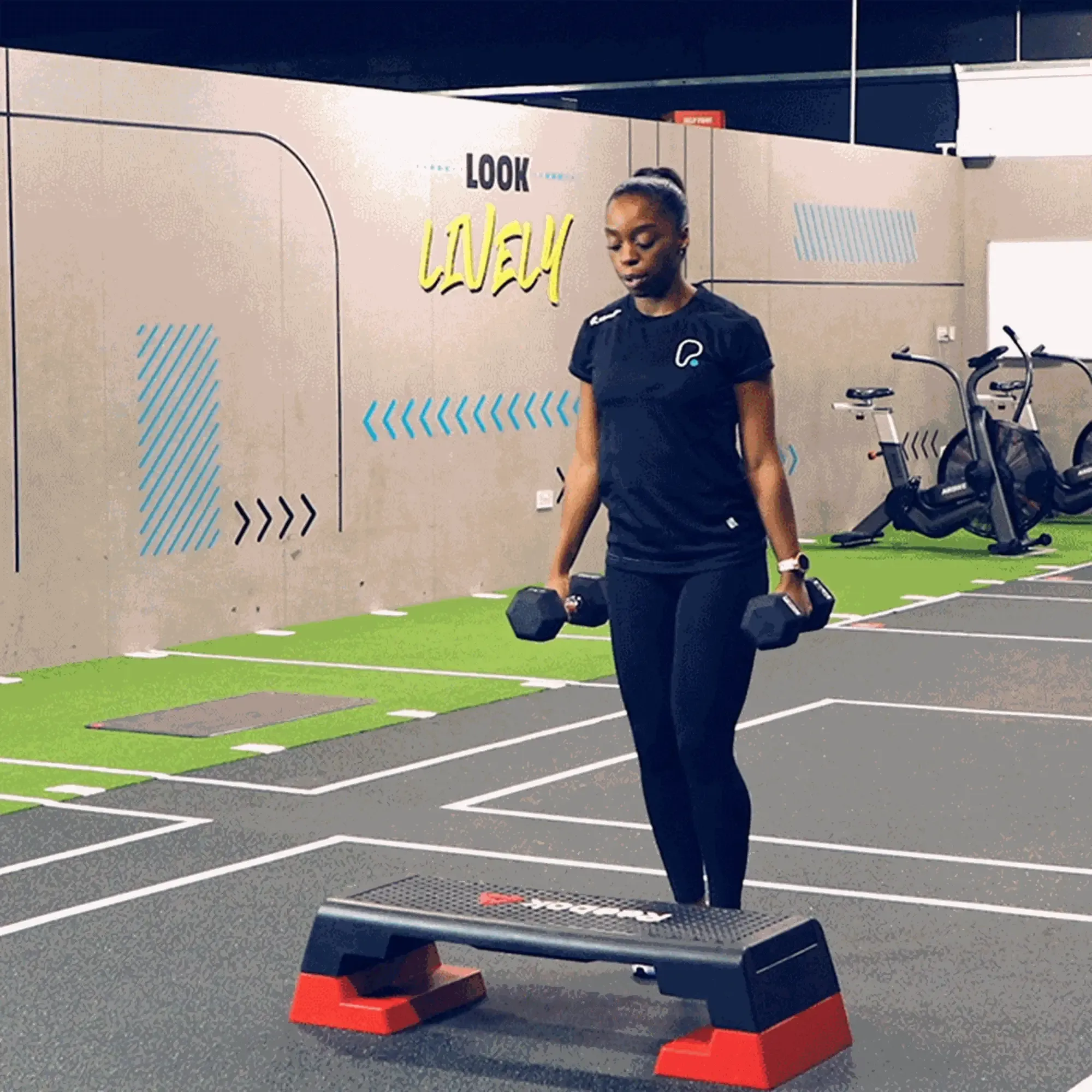 Woman exercising with dumbbells near a step platform in a gym with exercise bikes