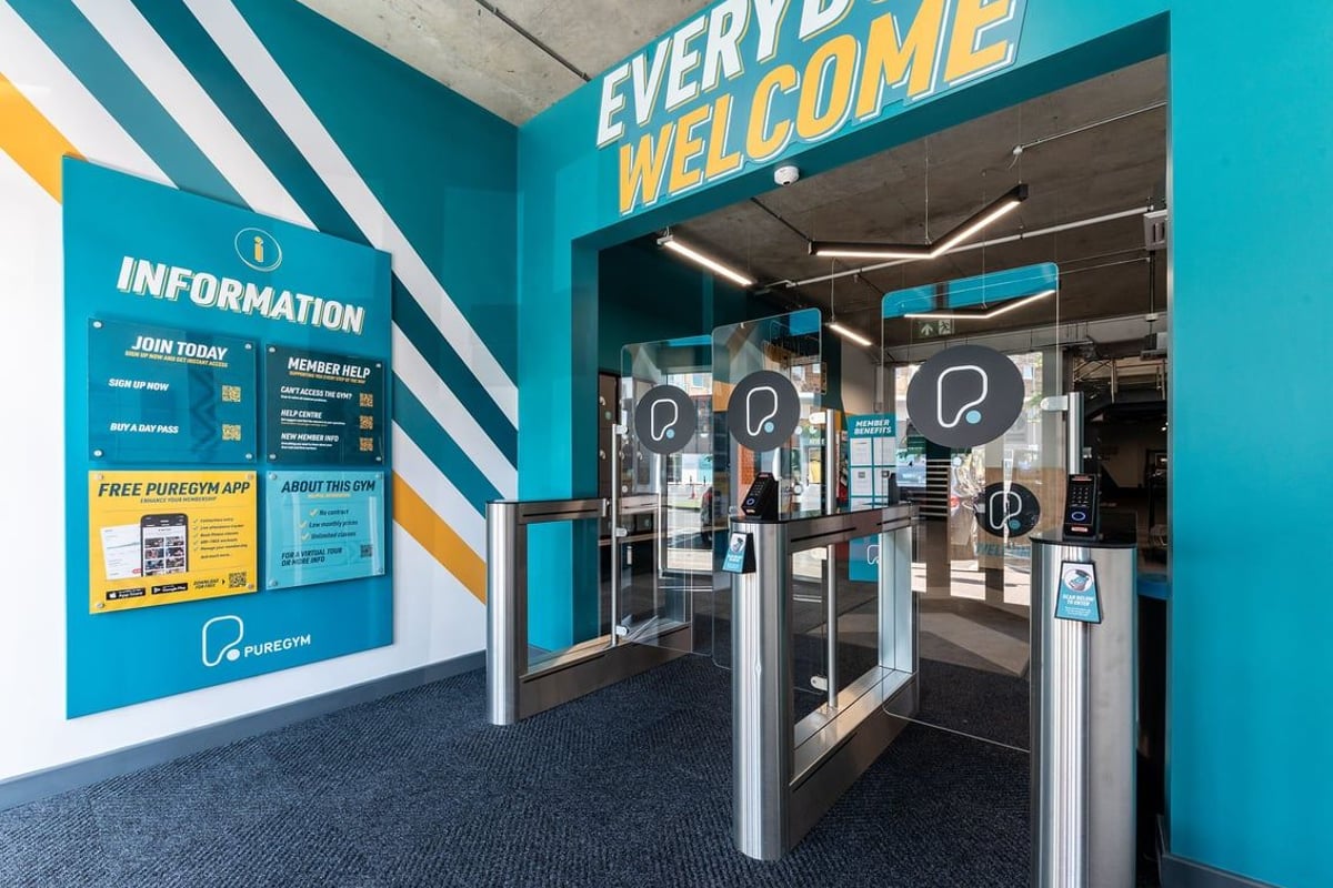 PureGym London Feltham: Welcome area with turnstiles, information displays, and "Every body welcome" signage.