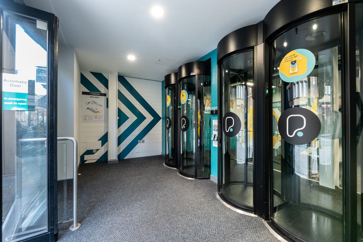 PureGym London Hammersmith Palais: Teal-coloured circular entry pods or kiosks in a corridor-like space.