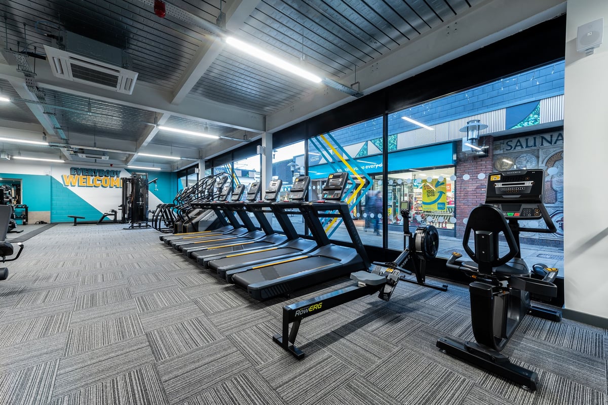 PureGym Droitwich Spa: Rows of treadmills, graphical backdrop, overhead lighting in a fitness studio.