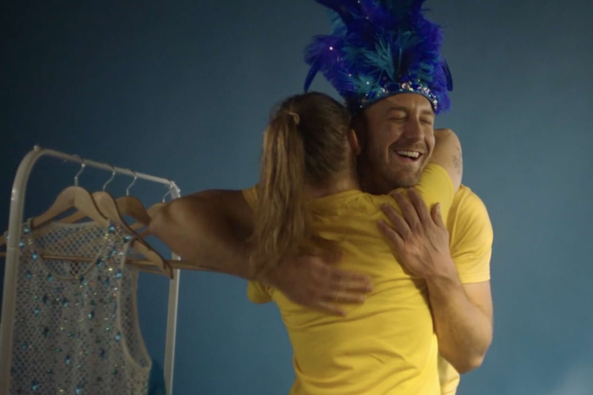 Two people in yellow shirts hugging, one wearing a blue feathered headpiece