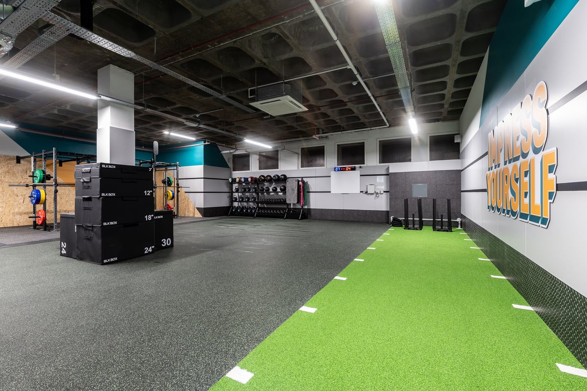 PureGym London Wood Green: Large open space with exercise turf, weight racks, mirrored wall, industrial ceiling.