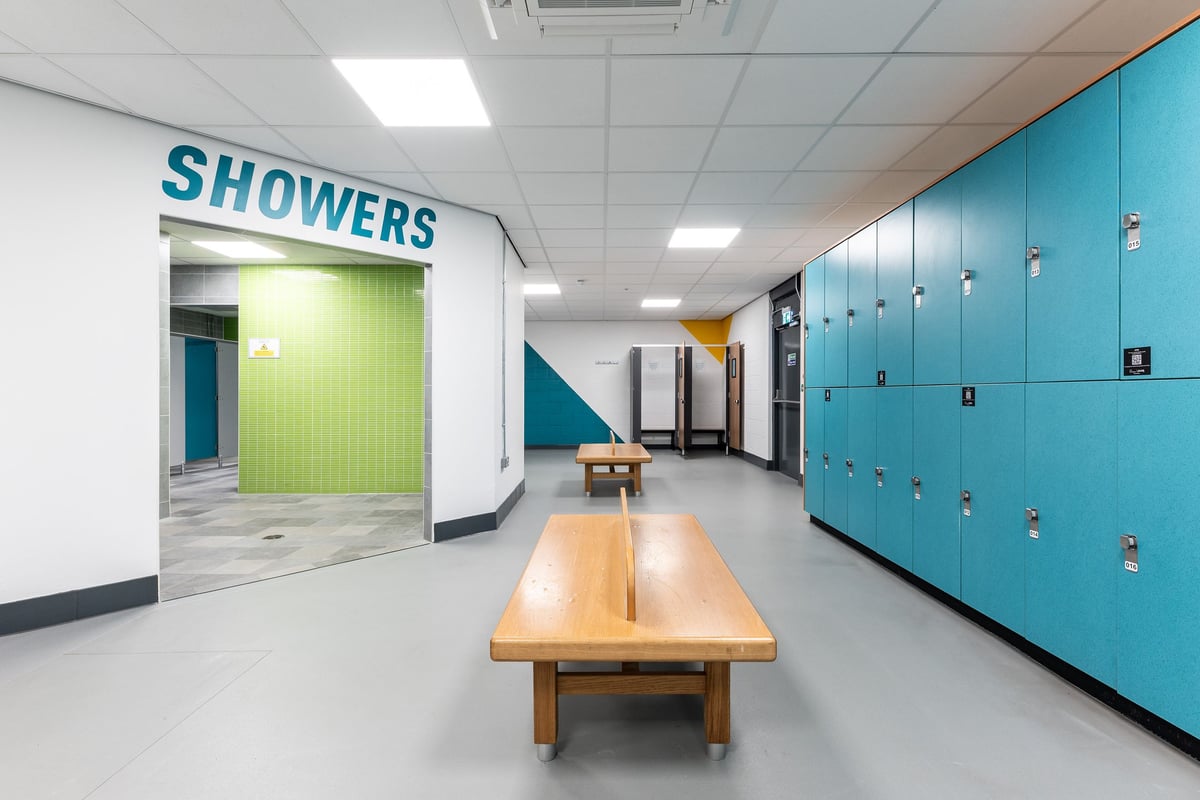 PureGym Sheffield Crystal Peaks: Shower area with teal lockers, wooden benches, and green curtain.