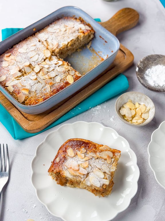 Baked almond cake with powdered sugar in a blue baking dish and a slice on a white plate