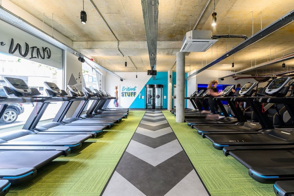 PureGym London Fulham: Rows of treadmills and ellipticals in a basement gym with chevron flooring pattern.